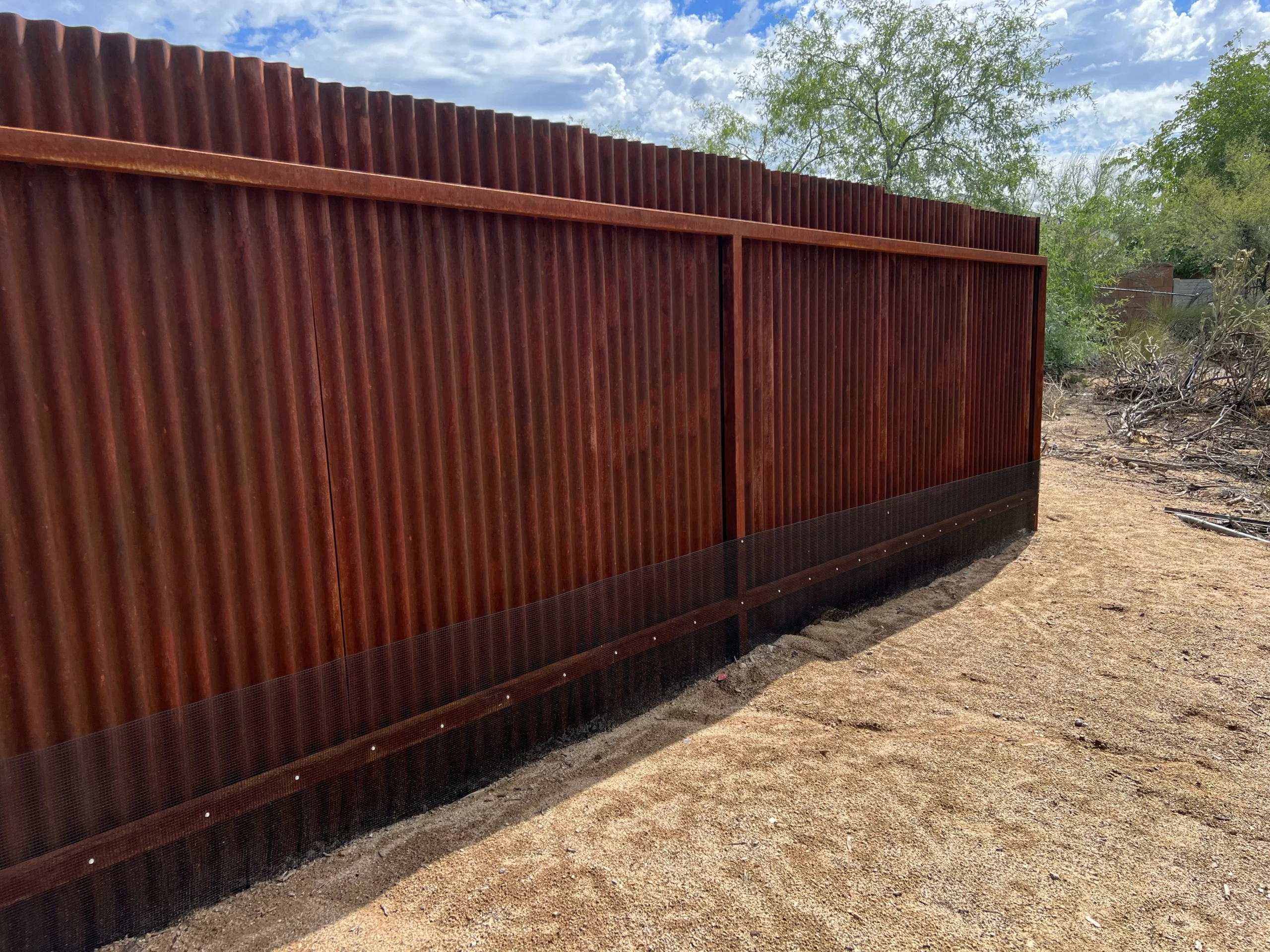 Black mesh barrier attached to an existing corrugated metal fence